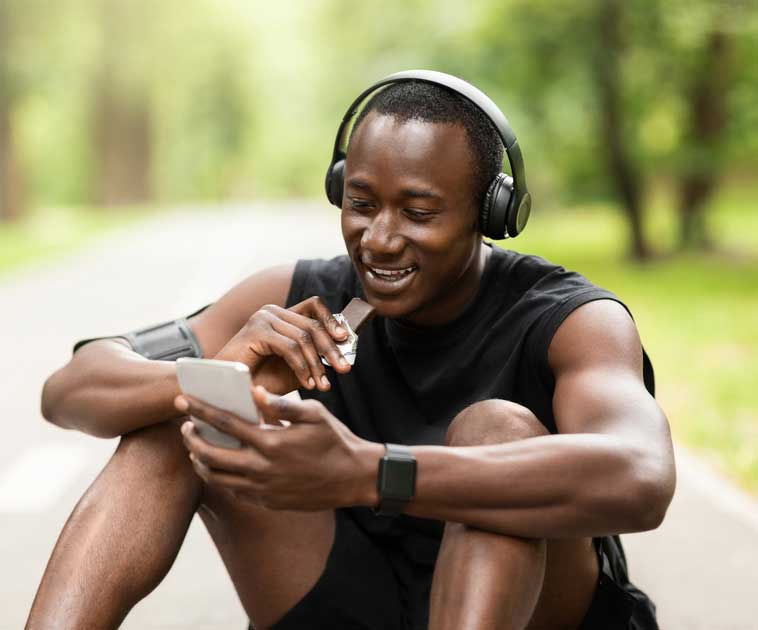 NCS Measurement - a man taking a break from running eating a granola bar, listening to music sitting by a path